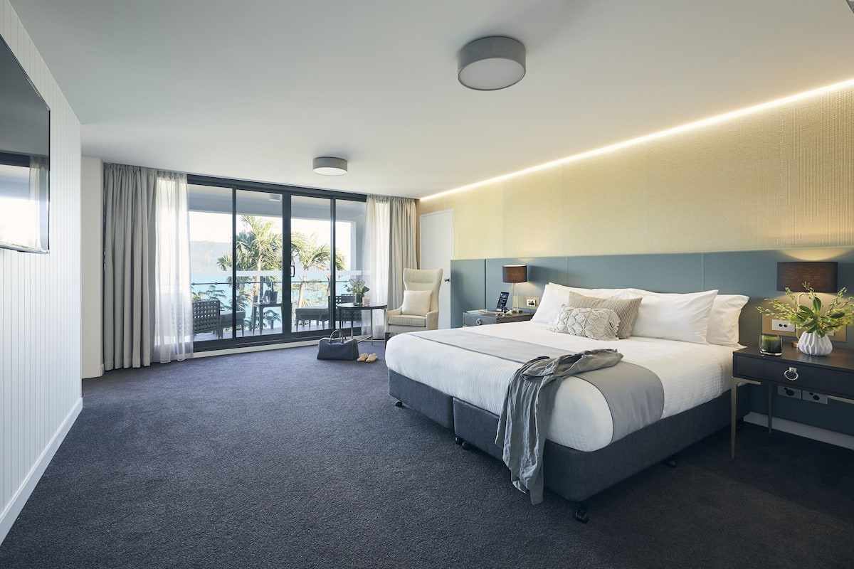 Habitación de hotel moderna con una cama grande, una mesita de noche, una lámpara y vistas al exterior.