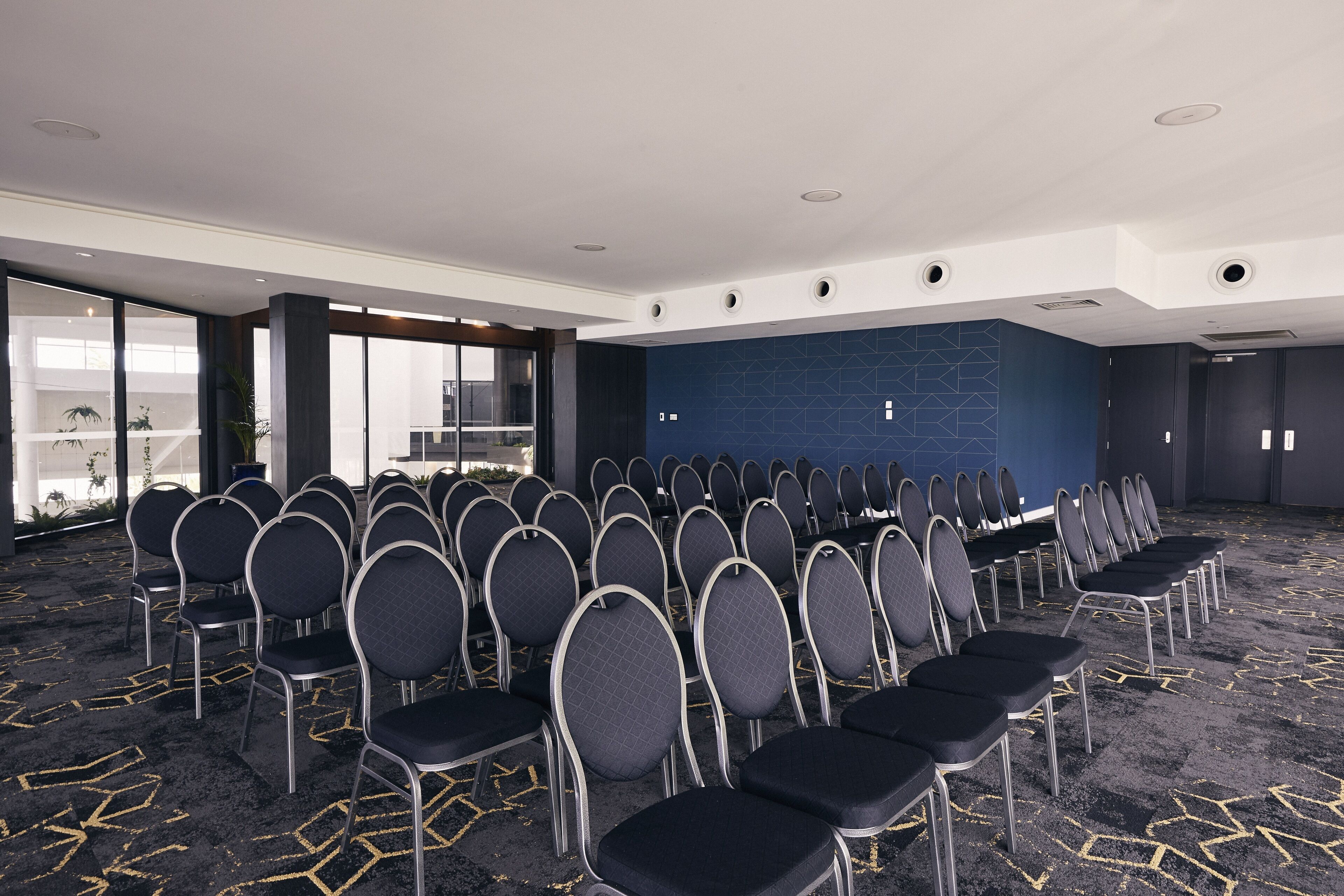 Une salle de conférence avec des rangées de chaises, un mur d’accent bleu et de grandes fenêtres.