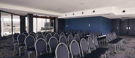 Une salle de conférence avec des rangées de chaises, un mur d’accent bleu et de grandes fenêtres.