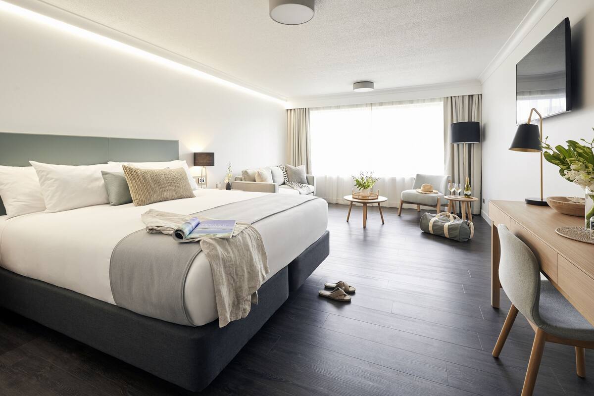 Una habitación de hotel moderna con una cama grande, un escritorio, una silla y una mesita de noche con lámpara.