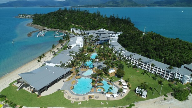 Vista aérea de un resort con varias piscinas, una playa y montañas al fondo.