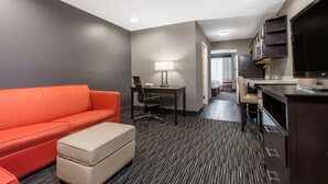 A hotel room with a sofa, a desk, a chair, a TV, and a kitchenette. - Hawthorn Extended Stay by Wyndham Columbus West (Columbus)