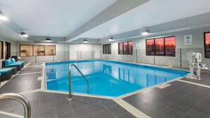 An indoor swimming pool with a clear view of the sunset through large windows, a lifeguard stand, and a seating area with blue cushions. - Hawthorn Extended Stay by Wyndham Columbus West (Columbus)
