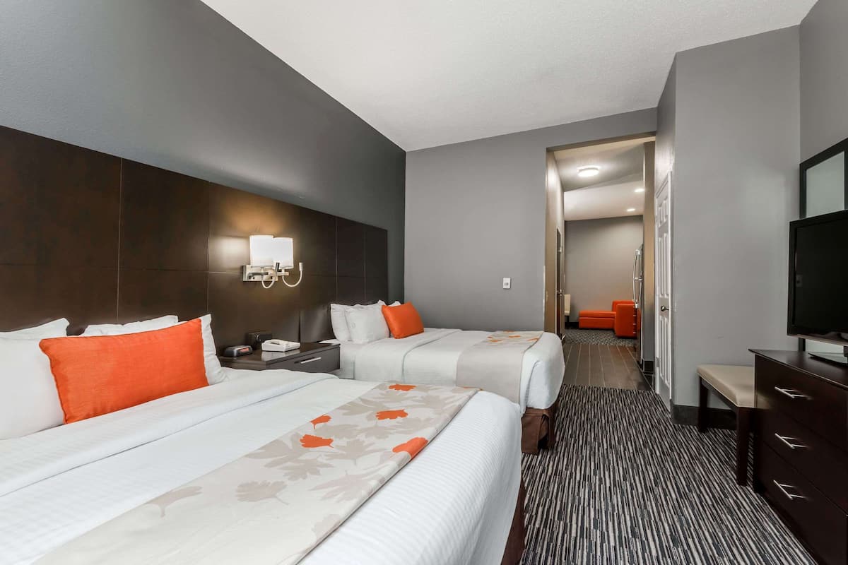 A hotel room with two beds, a TV, a desk, and a bathroom visible through an open door.