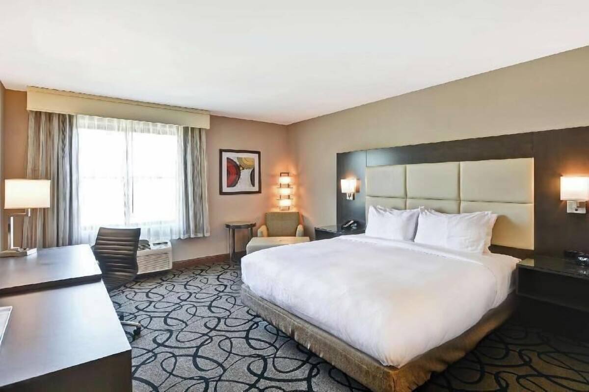 Una habitación de hotel con una cama grande, un escritorio, una silla, una mesita y una ventana con cortinas.