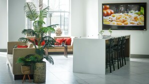 A modern living room with a sofa, a coffee table, a dining area with chairs, and a large window.