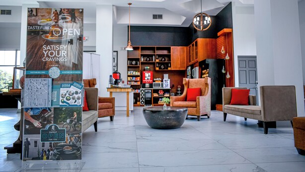 A spacious lobby with a modern design, featuring a large central table, comfortable seating, and a prominent 'Open' sign.