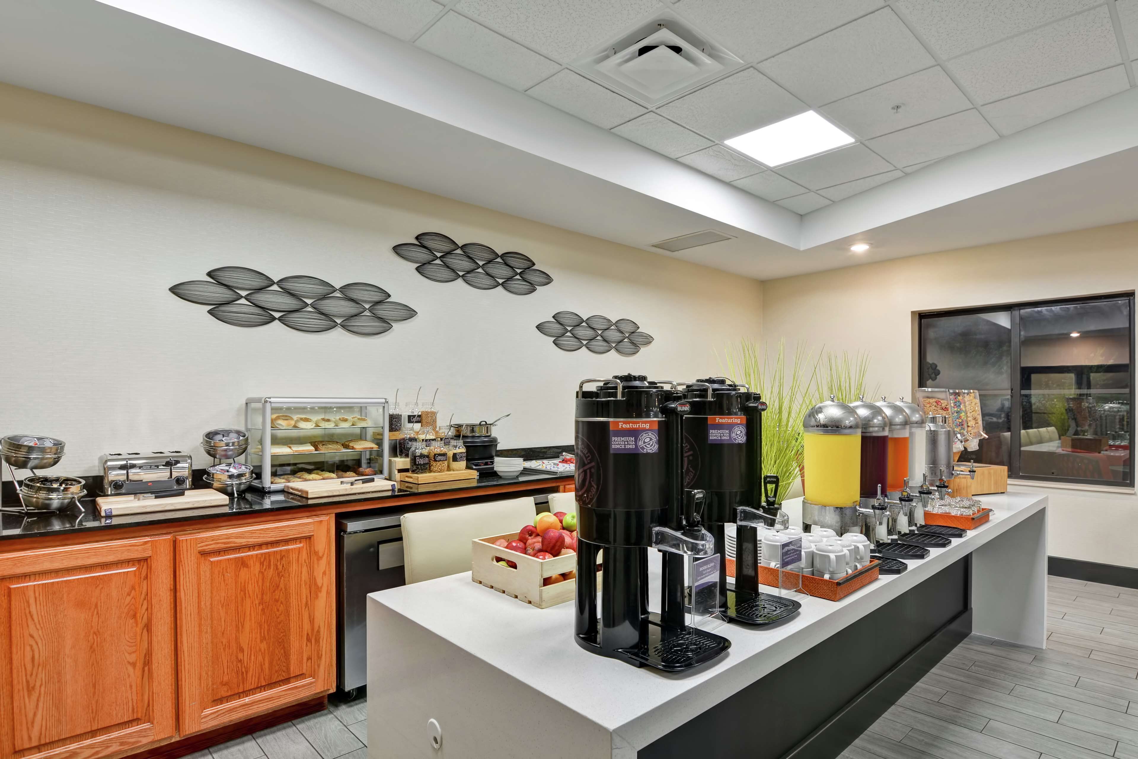 A breakfast bar with coffee machines, a fruit basket, and decorative wall art.