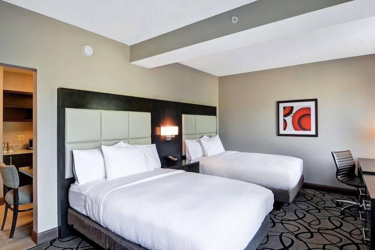 Habitación de hotel con dos camas, un escritorio, una silla y una lámpara en la pared.
