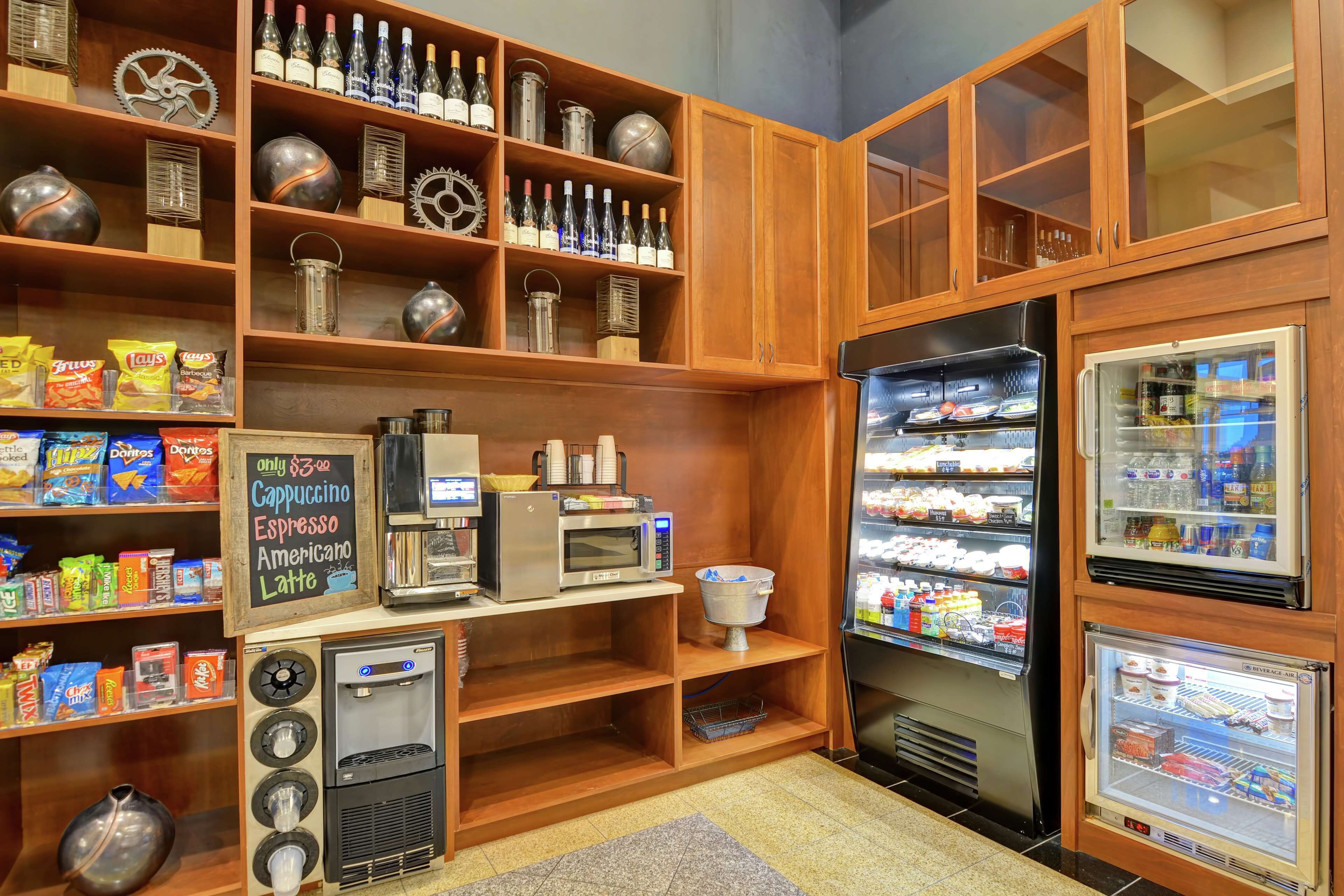 A self-service beverage station with a coffee machine, a soda dispenser, and a refrigerated display case with snacks.