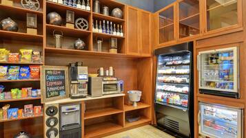 A self-service beverage station with a coffee machine, a soda dispenser, and a refrigerated display case with snacks.