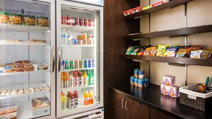 A refrigerated display with various food items and beverages, and shelves stocked with snacks and boxed goods. - Hawthorn Suites by Wyndham Las Vegas/Henderson (Henderson)