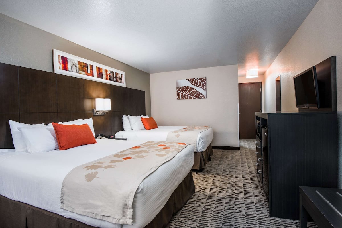 A hotel room with two beds, a TV, a desk, and artwork on the walls.