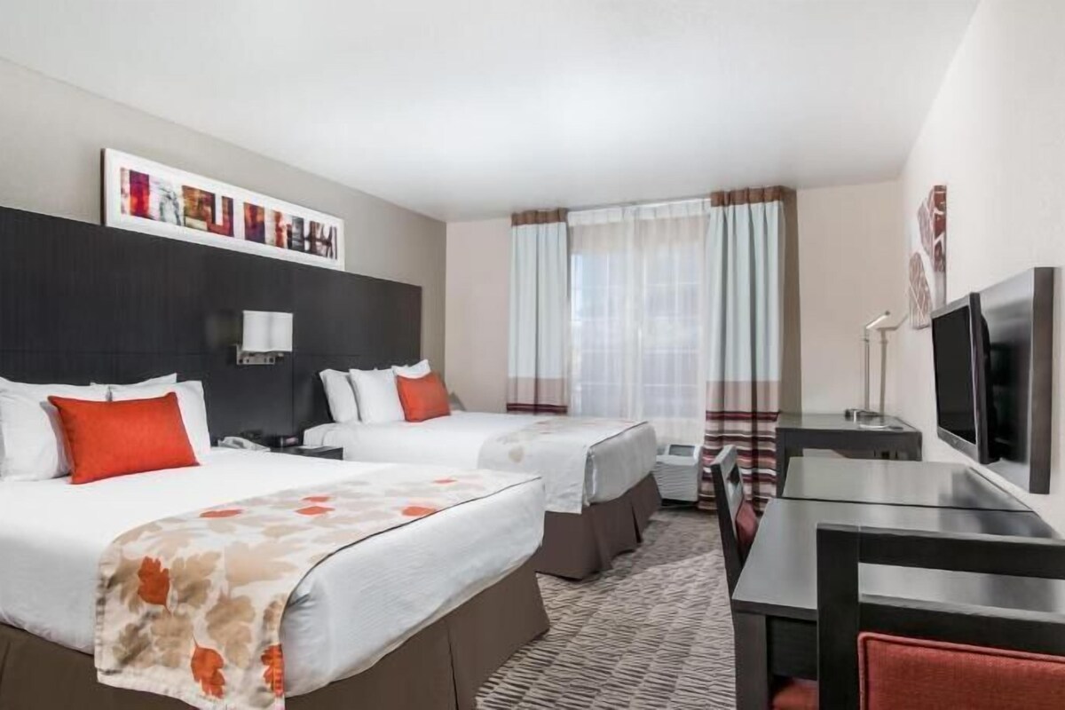 Habitación de hotel con dos camas, un escritorio, un televisor y una ventana con cortinas.