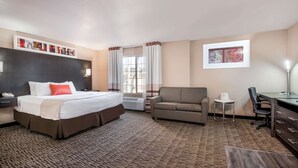 A hotel room with a large bed, a sofa, a desk, and a chair. There are two windows with curtains, a wall-mounted phone, and a framed picture on the wall. - Hawthorn Suites by Wyndham Las Vegas/Henderson (Henderson)