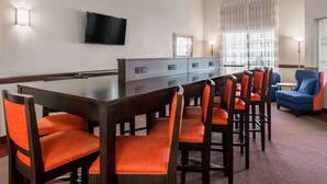 A hotel room with a dining table, chairs, a flat-screen TV, a mirror, and a window with curtains. - Hawthorn Suites by Wyndham Las Vegas/Henderson (Henderson)