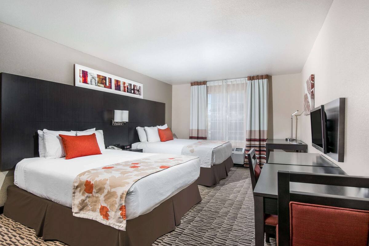 A hotel room with two beds, a desk, a TV, and a window with curtains.
