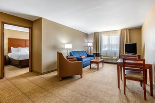 Una habitación de hotel con cama, sofá azul, silla de madera, una mesita y televisor.