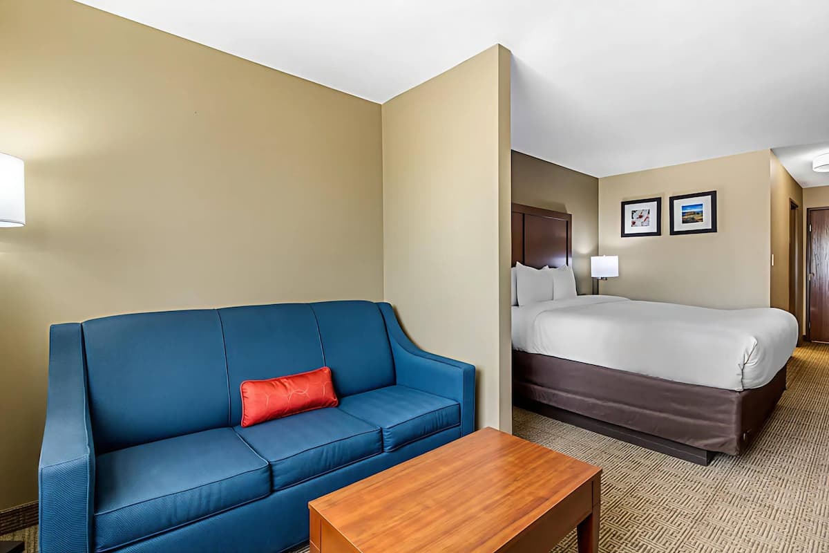 A hotel room with a blue sofa, a wooden coffee table, a bed, and two framed pictures on the wall.