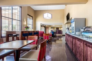 A hotel dining area with tables and chairs, a counter with a beverage dispenser, and a large window.