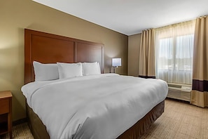 A hotel room with a large bed, a bedside table, a lamp, and a window with curtains.