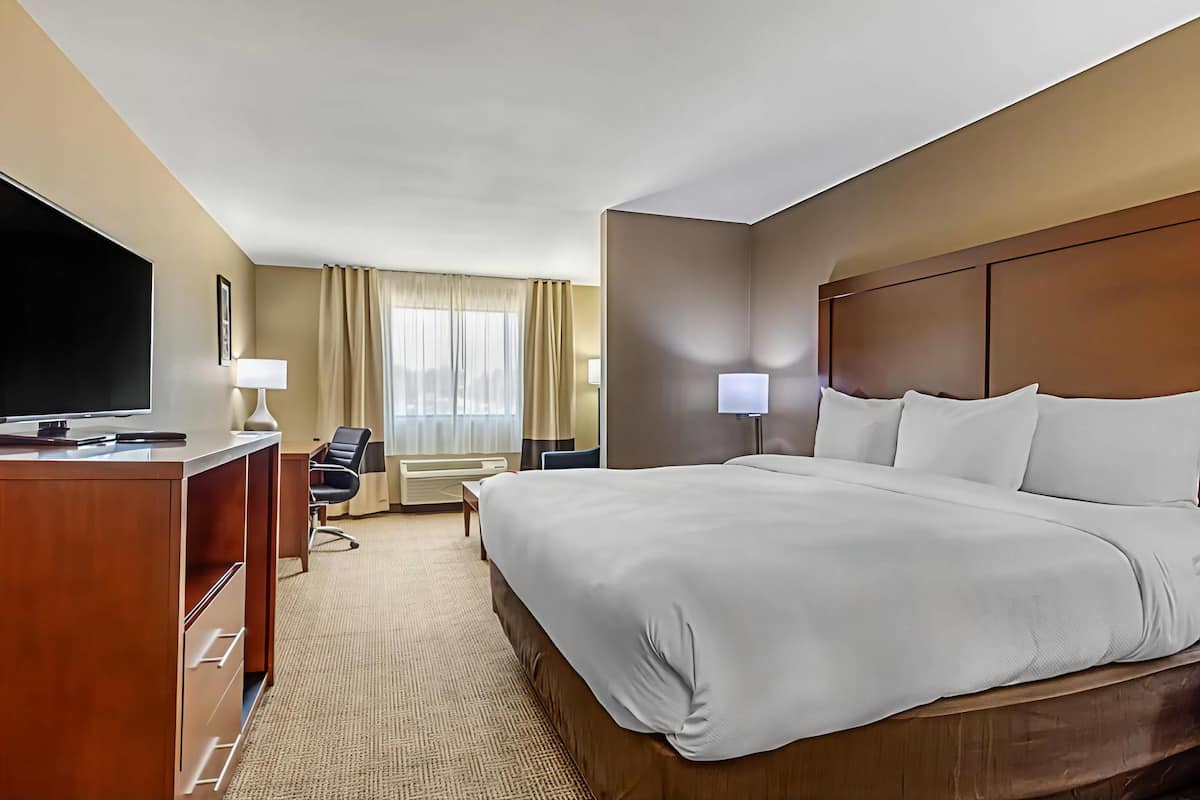 A hotel room with a large bed, a desk with a TV, a chair, and two lamps.