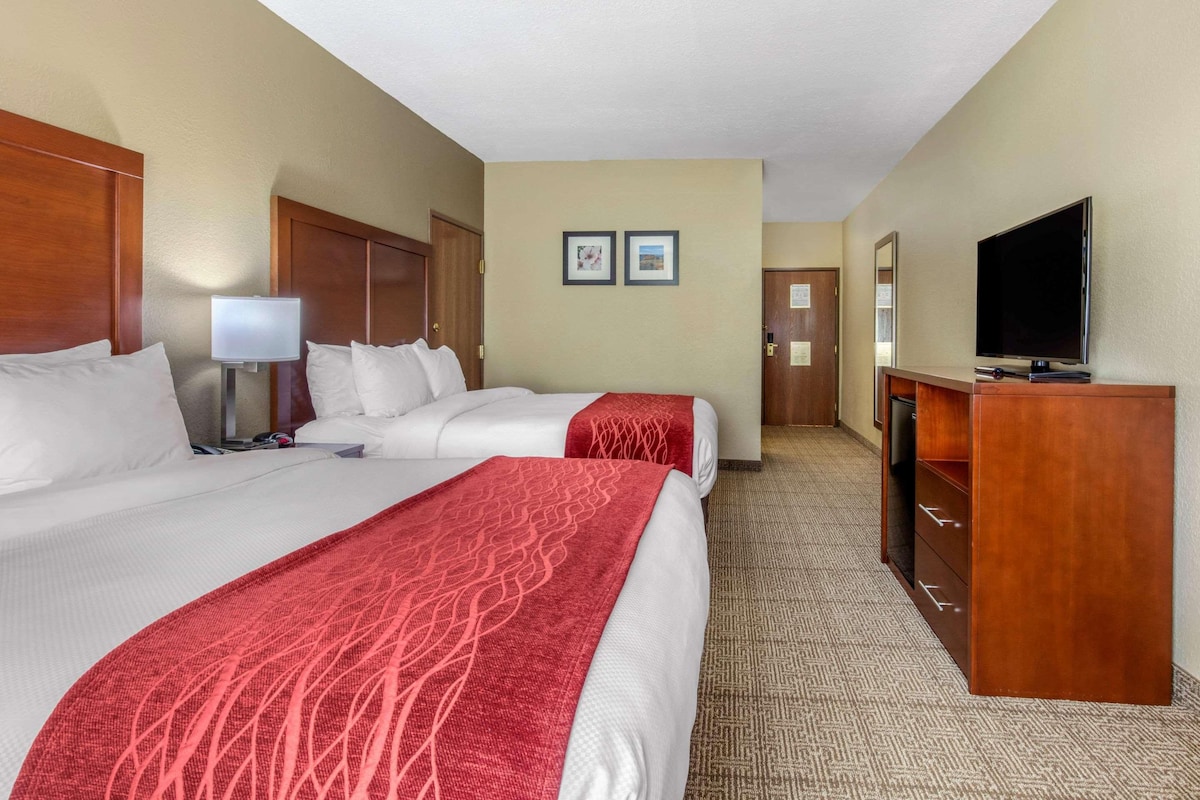 A hotel room with two beds, a desk, a TV, and a lamp.