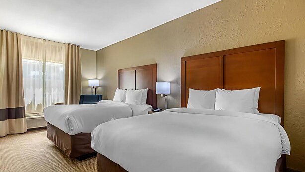 A hotel room with two beds, each with a wooden headboard and white bedding. There are two bedside tables with lamps, and a window with curtains. - Comfort Inn & Suites McComb (McComb)