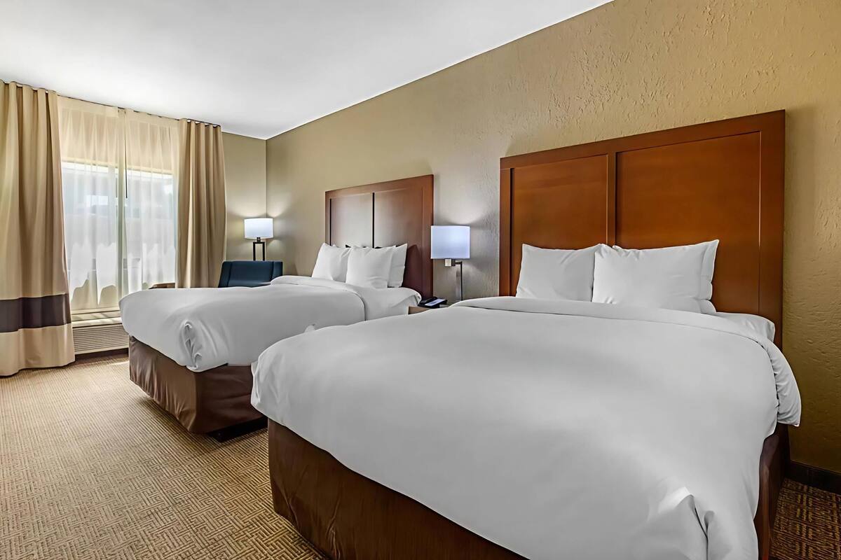 A hotel room with two beds, a desk, a chair, and a large window with curtains.