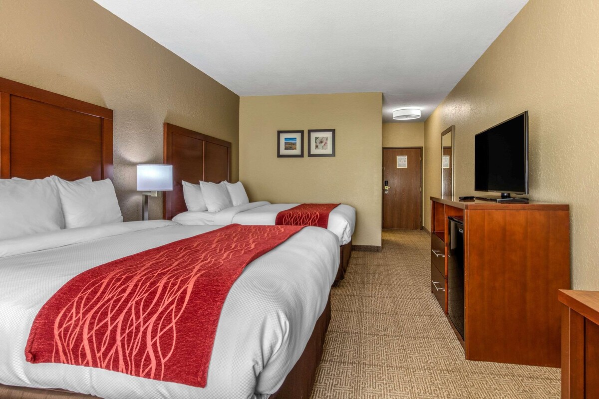 A hotel room with two beds, a desk, a television, and a lamp.