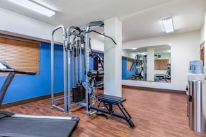 Une salle de sport équipée de matériel d’exercice, d’un distributeur d’eau et d’un miroir qui reflète la pièce.