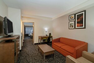 Una habitación de hotel con televisión, escritorio, silla, sofá y alfombra estampada.