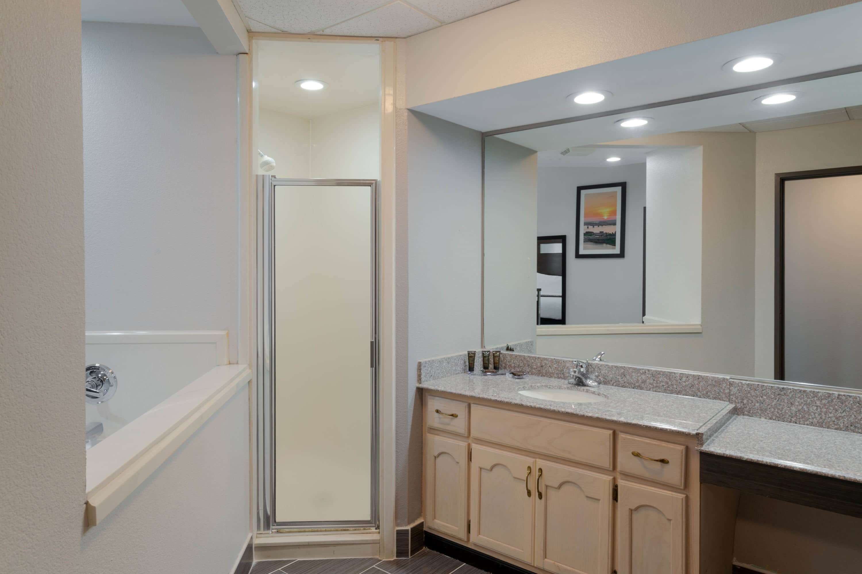 A modern bathroom with a glass-enclosed shower, a large mirror, and a vanity with a sink and cabinet.