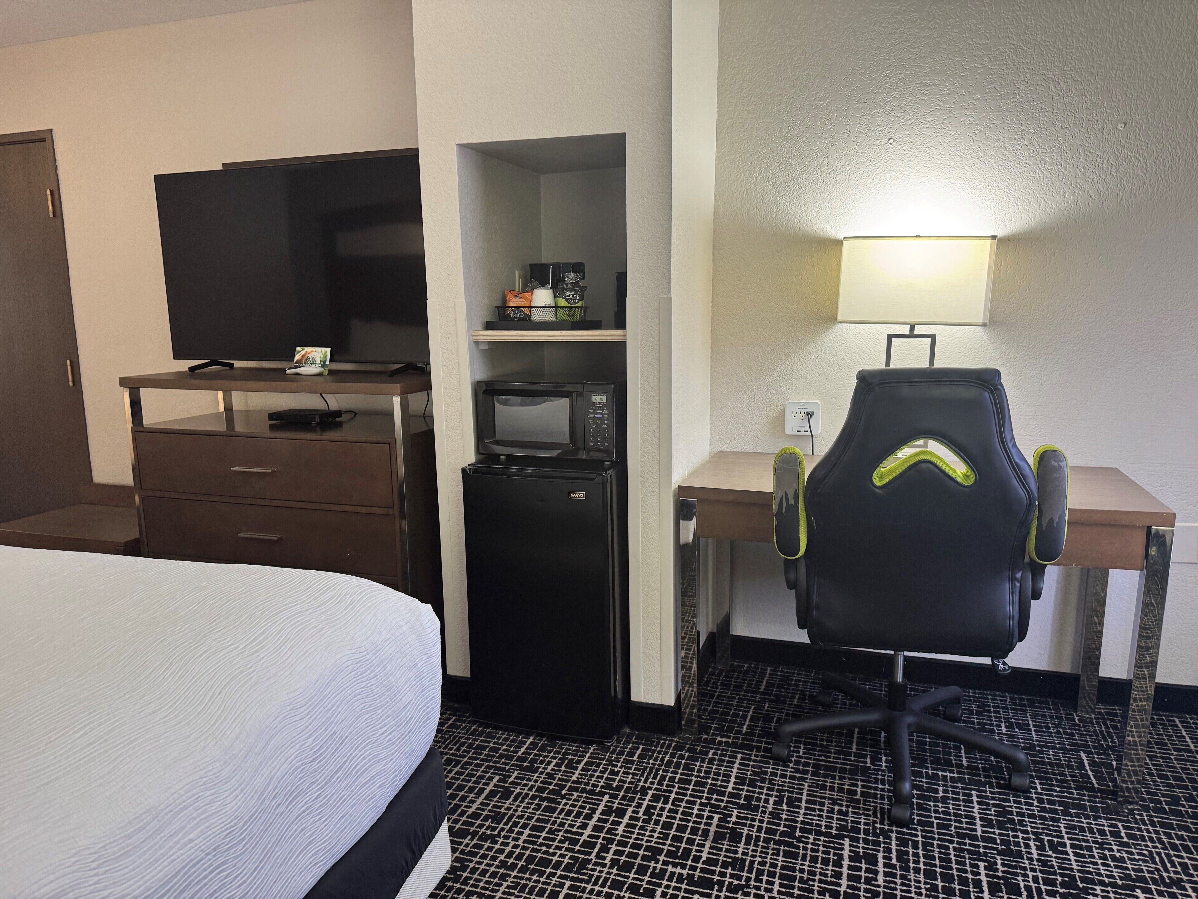 Una habitación de hotel con cama, escritorio con computadora, microondas y televisión.