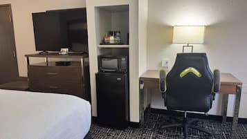 A hotel room with a bed, a desk with a computer, a microwave, and a TV.
