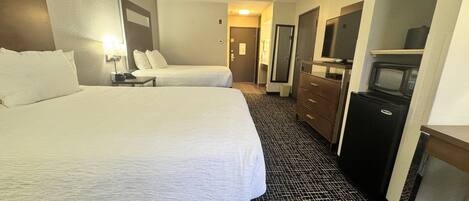 A hotel room with two beds, a dresser, a television, and a microwave.