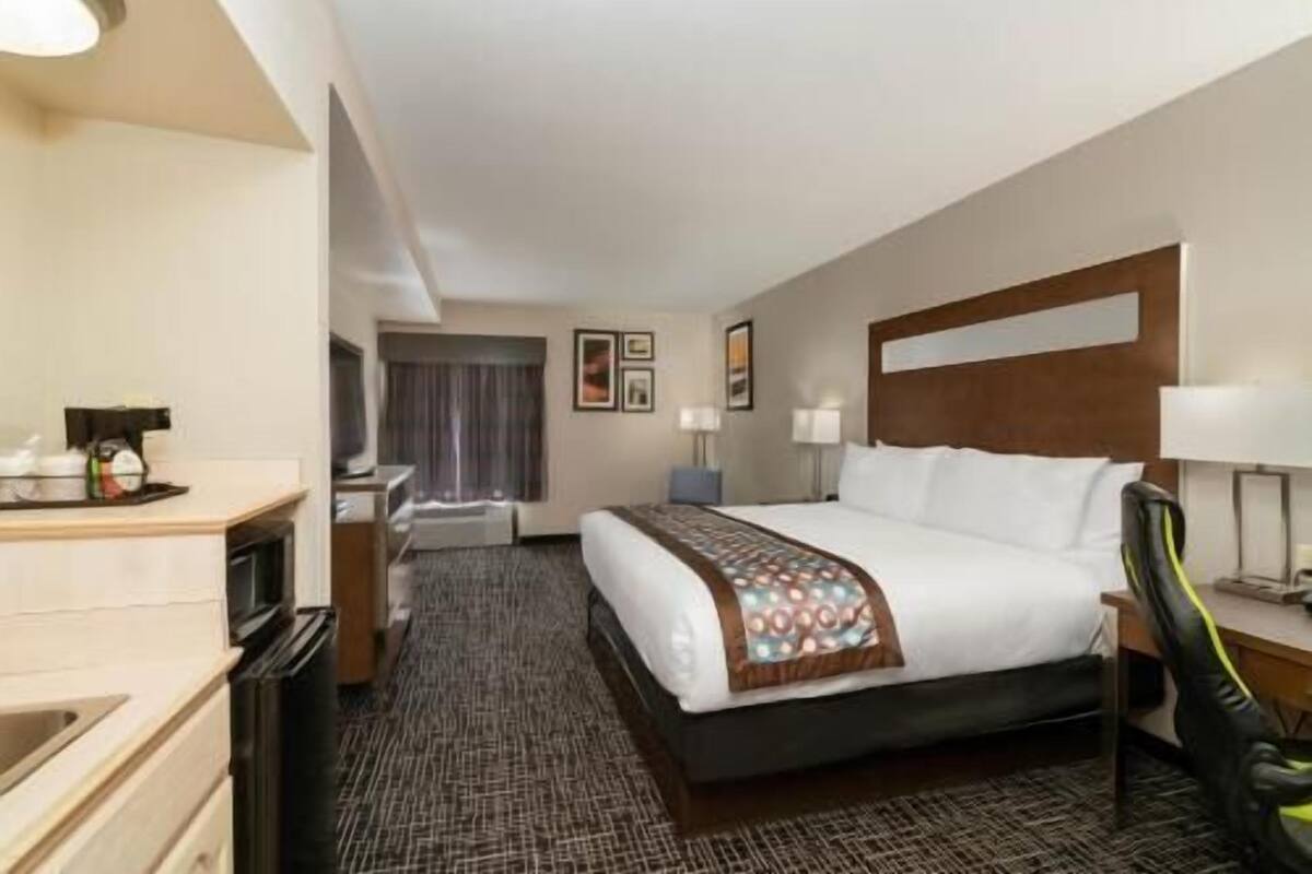 A hotel room with a bed, bedside tables, a desk, a chair, a TV, and a window with curtains.