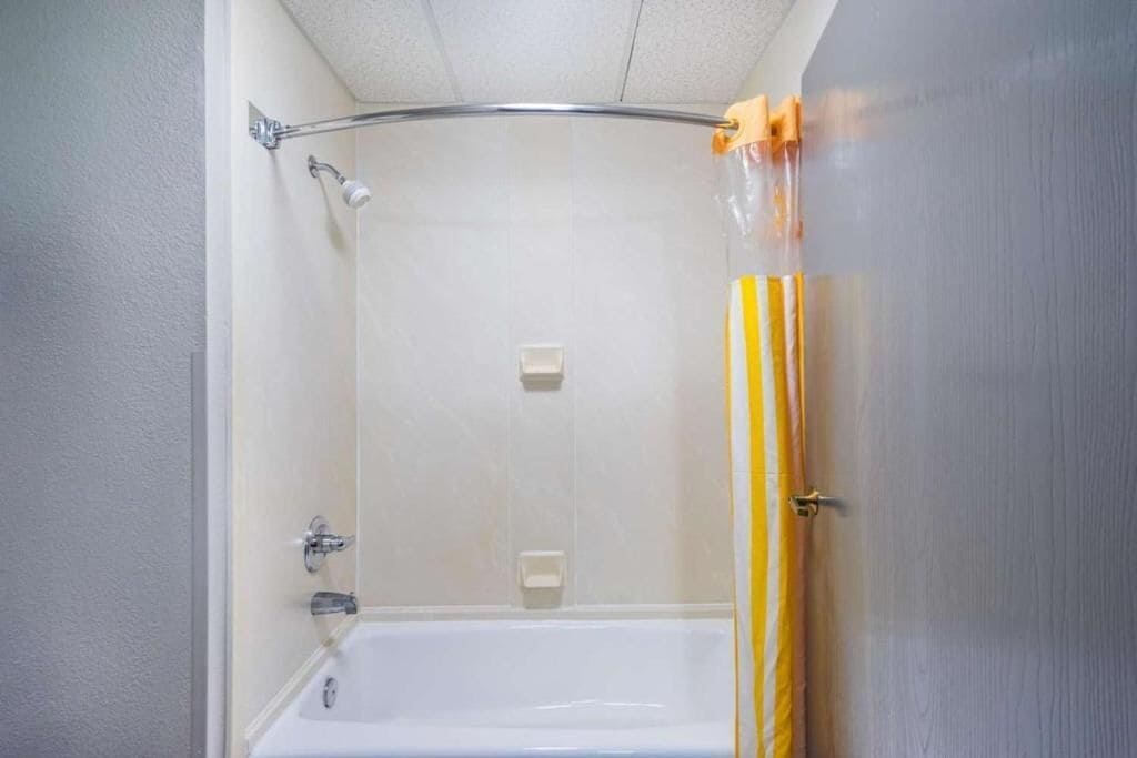 Un baño con ducha, bañera y cortina de baño a rayas amarillas y blancas.