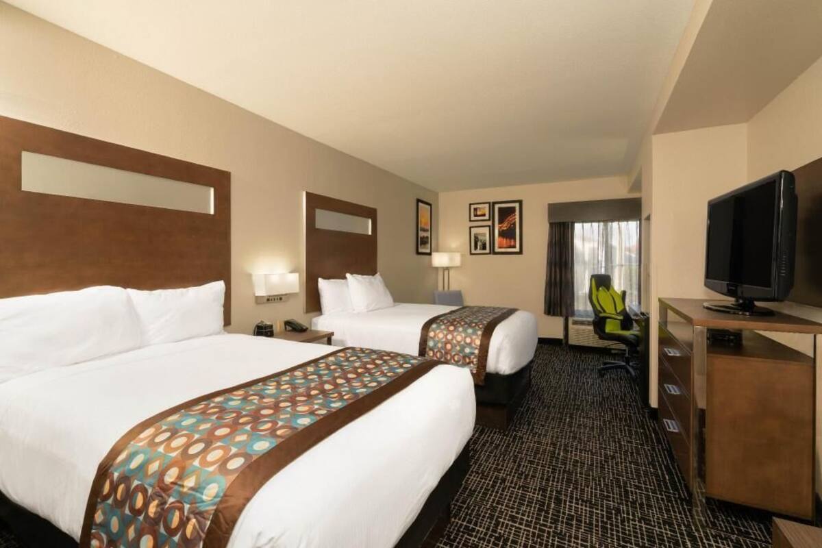 A hotel room with two beds, a desk, a TV, and a chair.