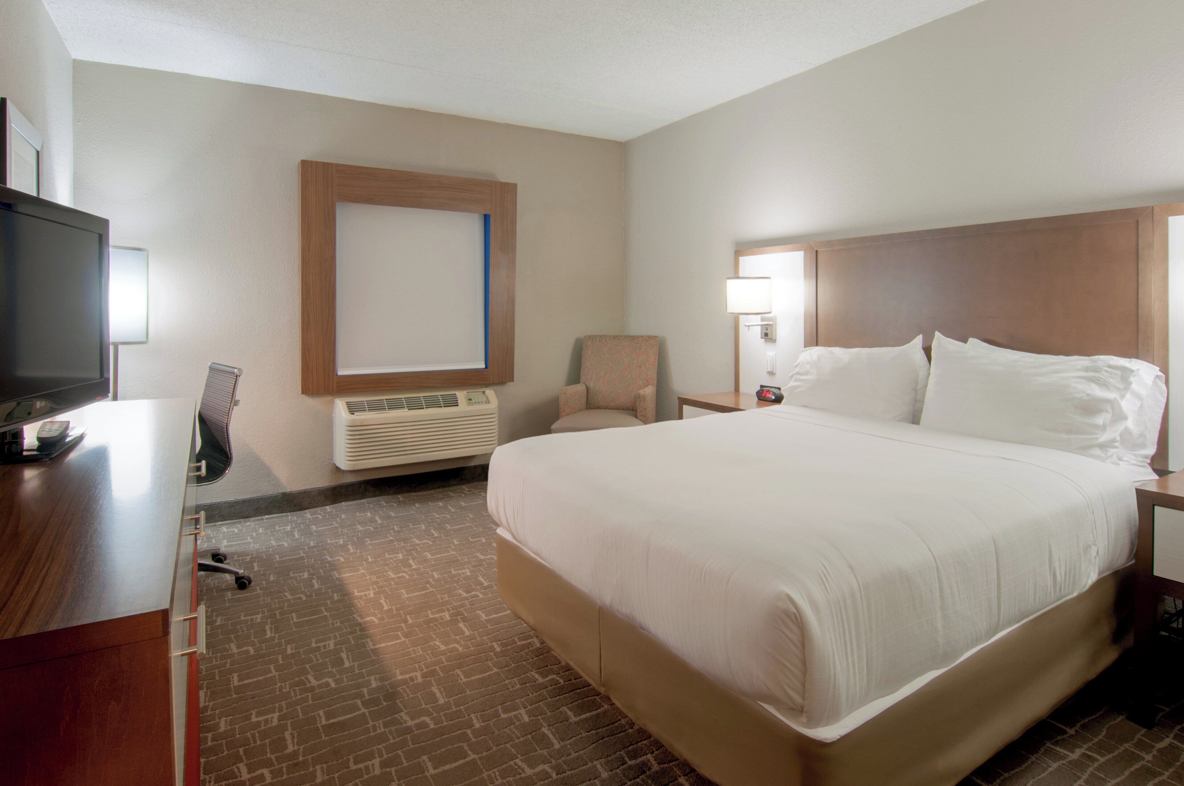 Une chambre d’hôtel avec un grand lit, un bureau avec une télévision, une chaise, une table de chevet avec une lampe et un climatiseur fixé au mur.