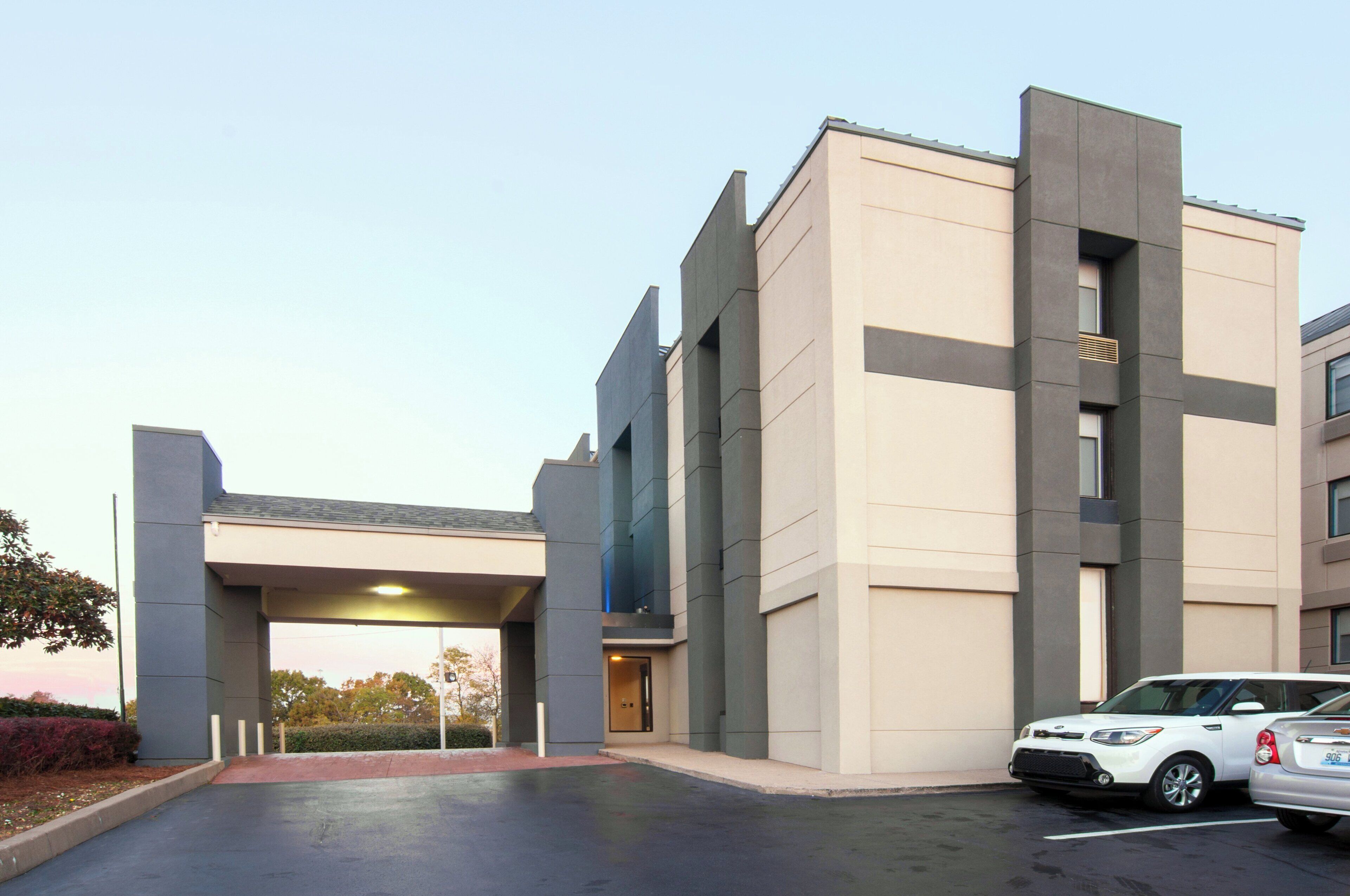 A modern building with a flat roof and a covered entrance. There are two cars parked in front.