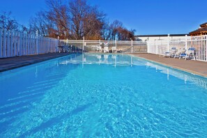 A clear swimming pool with a white fence, lounge chairs, and a view of trees and a building in the background. - Holiday Inn Express Hotel & Suites Spence Lane by IHG (Nashville)