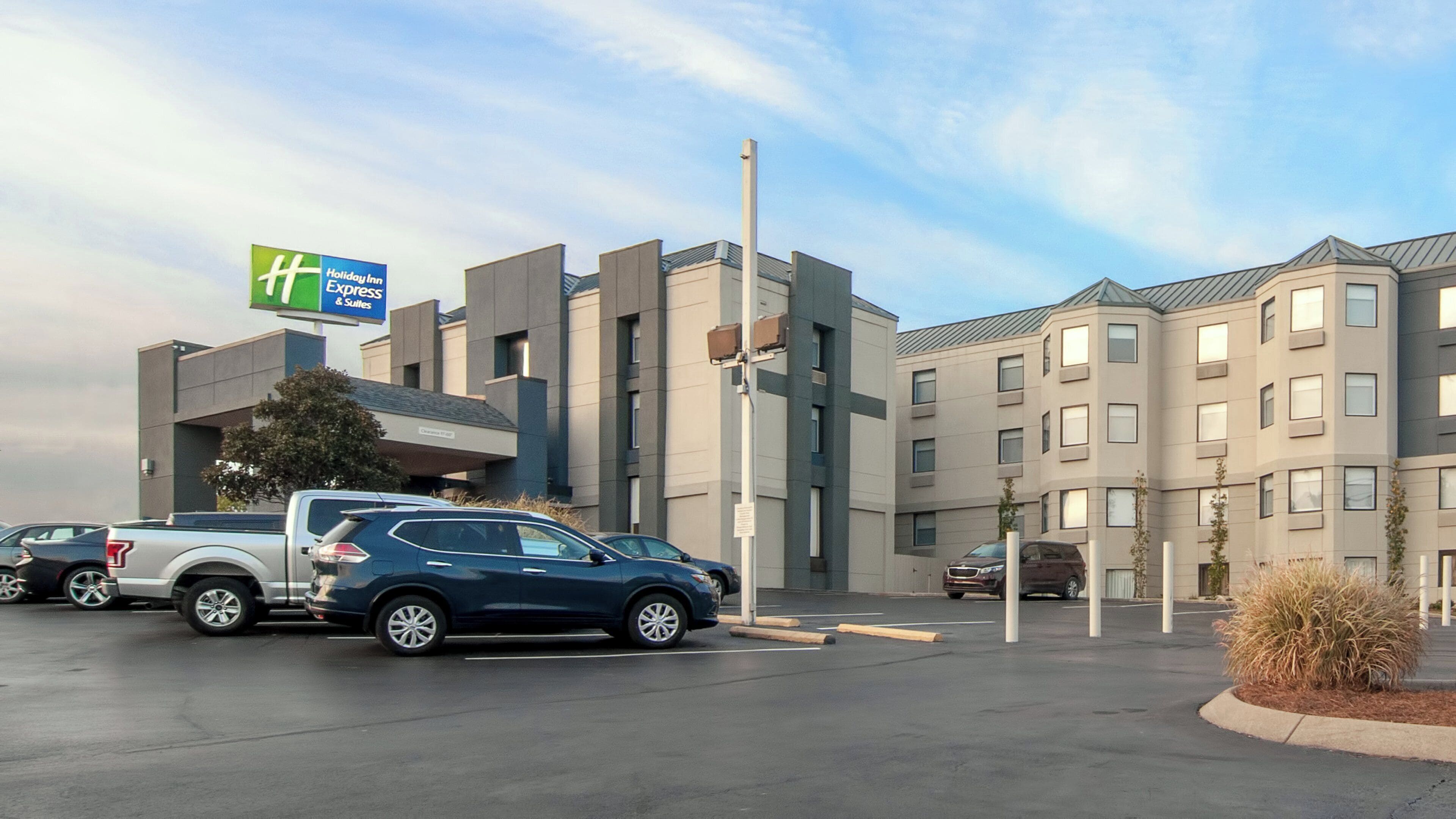 A Holiday Inn Express & Suites with a parking lot, a building with a flat roof, and a clear sky.