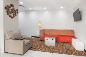 A modern living room with a beige sofa, a red sofa, a small table, and a flat-screen TV mounted on the wall. - Holiday Inn Express Hotel & Suites Spence Lane by IHG (Nashville)