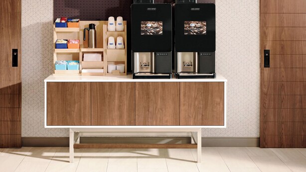 A modern coffee station with two coffee machines, a coffee grinder, and various coffee-related items on shelves. - Holiday Inn Express Hotel & Suites Spence Lane by IHG (Nashville)