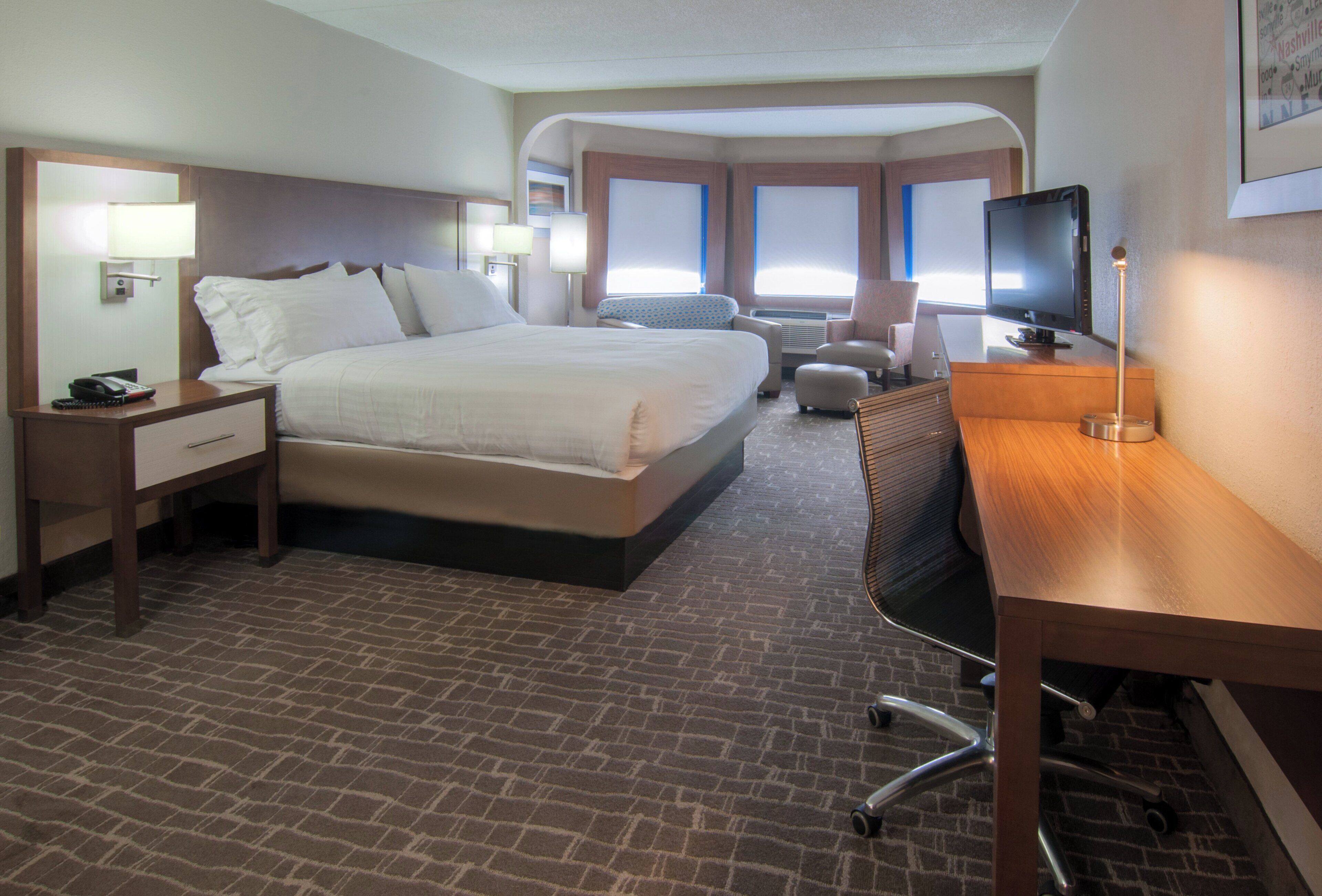 A hotel room with a large bed, a desk, a chair, a TV, and a window.