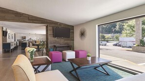 A modern hotel lobby with a seating area, a flat-screen TV mounted on the wall, and a view of the parking lot through large windows. - La Quinta Inn & Suites by Wyndham Portland NW (Portland)