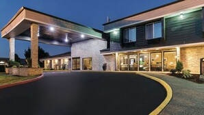 A modern hotel with a covered entrance, outdoor seating area, and a well-lit facade. - La Quinta Inn & Suites by Wyndham Portland NW (Portland)