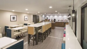 A modern dining area with a long counter, multiple seating options, and a kitchen in the background. - La Quinta Inn & Suites by Wyndham Portland NW (Portland)