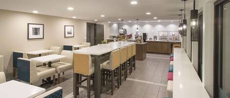 A modern dining area with a long counter, multiple seating options, and a kitchen in the background.